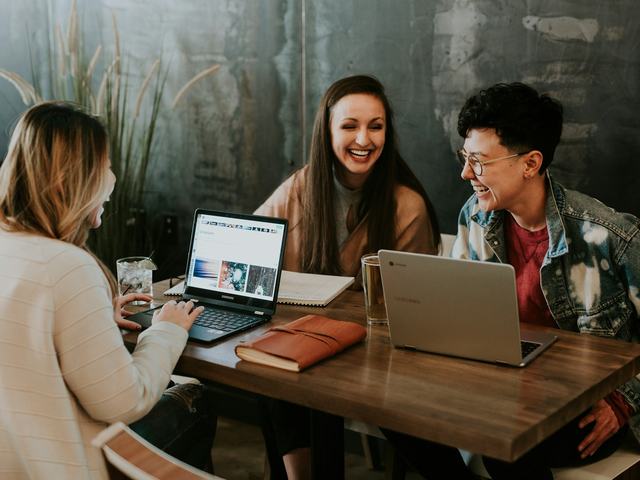 Three colleagues laughing together while working at a shared desk